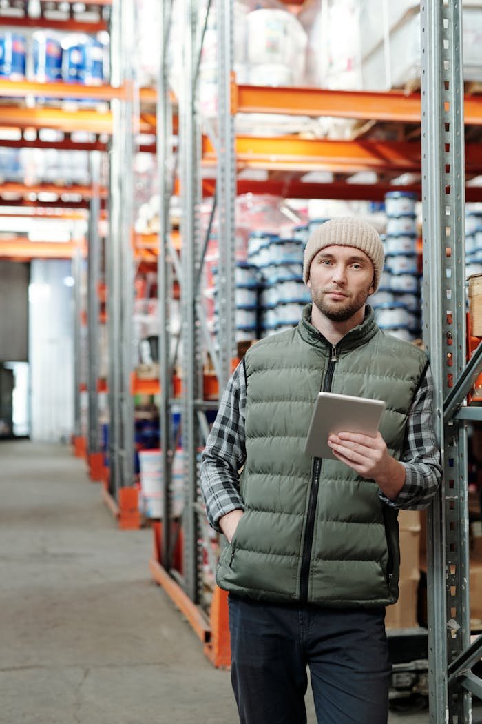 Man wearing beanie holds tablet in industrial warehouse setting.